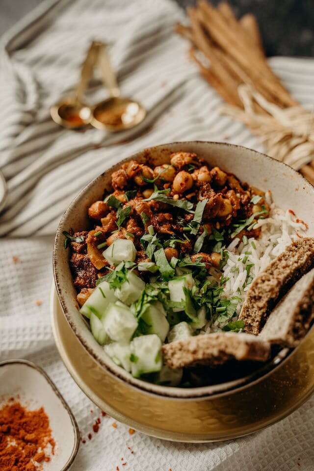 A bowl of balanced holiday food featuring rice, seasoned chickpeas, fresh cucumber, herbs, and whole-grain bread, arranged on a rustic table setting.